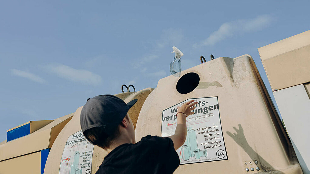 Ein Junge wirft eine Kunststoffverpackung den Container für Verkaufsverpackungen.